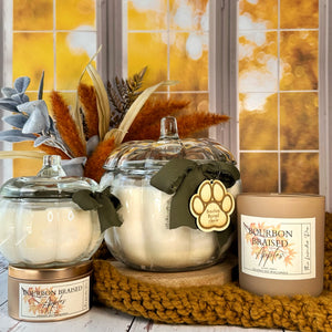 Group of candles on wooden surface with a fall day through a window pane in the background. Image features yellow knitted fabric and fall foliage.
