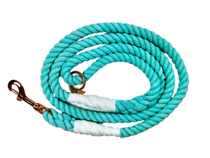Aqua blue colored rope dog leash with rose gold hardware and charm coiled up a white background.