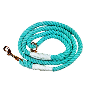 Aqua blue colored rope dog leash with rose gold hardware and charm coiled up a white background.