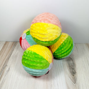 Squeaky ball dog toy wrapped in fabric to look like a beach ball. The toys are sitting on a light wood surface with a white background. 