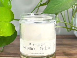Candle in a glass jar with a label on a wooden surface, surrounded by green leaves.
