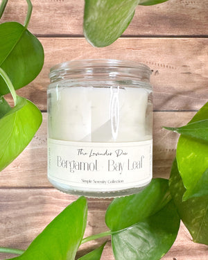 Candle in a clear jar with a label on a wooden surface with green leaves in the background