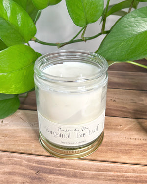 Candle in a glass jar with a label on a wooden surface with green leaves in the background