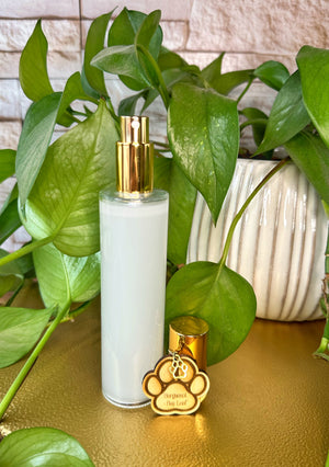Clear bottle room spray with gold cap on a wooden surface with green plants in the background
