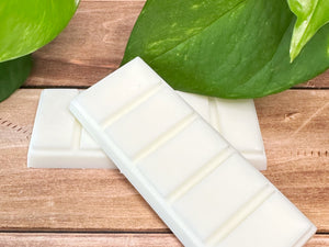 Two white wax melt bars on a wooden surface with green leaves in the background