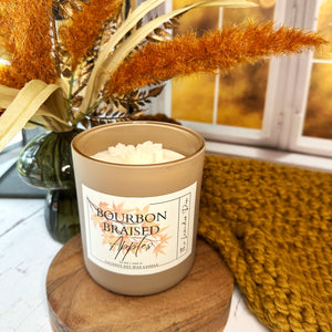 Candle labeled 'Bourbon Braised Apples' on a wooden coaster with decorative elements.