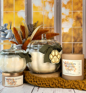 Candle jars with paw print design and autumn-themed label on a wooden surface.