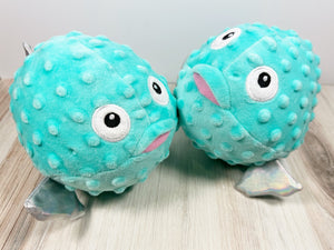 Two plush dog toys designed to resemble pufferfish with blue bodies and cartoon faces. 