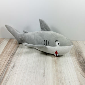 Plush dog toy designed to look like a shark. The toy is sitting on a light wooden surface against a white background