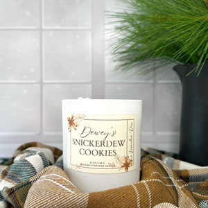 Candle labeled 'Dewey's Snickerdew Cookies' on a checkered fabric with a snowy background