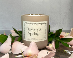 Candle labeled 'Dewey's Spring' surrounded by flowers on a wooden surface.