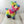 A colorful plush dog toy resembling a piñata. The toy sits on a light wooden surface with a white background. 