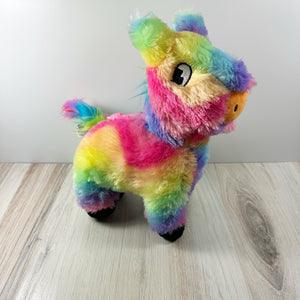 A colorful plush dog toy resembling a piñata. The toy sits on a light wooden surface with a white background. 