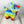 Plush dog toy resembling a colorful piñata. The toy is sitting on a light wooden surface with a white background. 