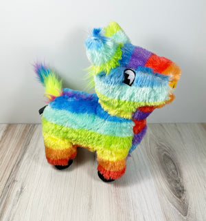 Plush dog toy resembling a colorful piñata. The toy is sitting on a light wooden surface with a white background. 