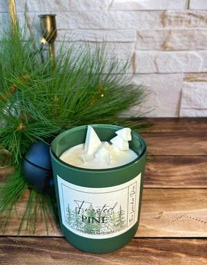 Green jar candle labeled 'Frosted Pine' on a wooden surface with decorative background