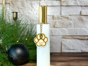 White and gold bottle room spray with paw charm on a wooden surface with decorative items.