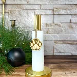 White and gold bottle room spray with paw charm on a wooden surface with decorative items.