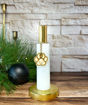 White and gold bottle room spray with paw charm on a wooden surface with decorative items.