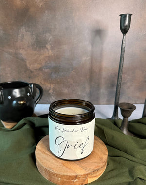Candle jar labeled 'Grief' on a wooden stand with a textured wall background