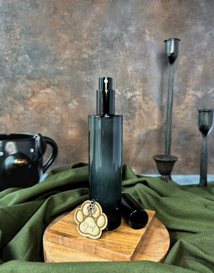 Black bottle room spray with black lid and a paw print charm on a wooden stand and fabric details
