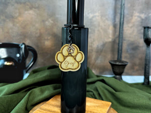 Black bottle room spray with black lid and a paw print charm on a wooden stand with fabric details