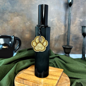 Black bottle room spray with black lid and a paw print charm on a wooden stand with fabric details
