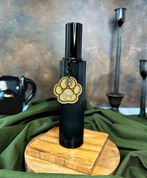 Black bottle room spray with black lid and a paw print charm on a wooden stand with fabric details