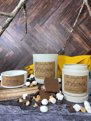 Photo showing all available sizes of our S'mores candle. Surrounding the candles are tree branches, chocolate chunks, and marshmallows. 