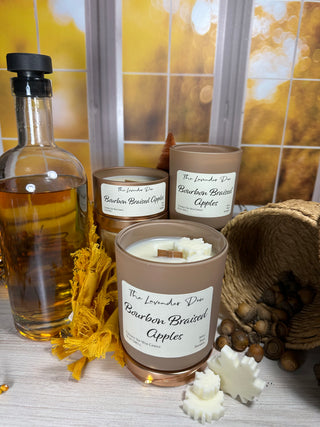 Picture showing all available sizes of our Bourbon Braised Apples Candles. Surrounding the candles is a bottle of bourbon and acorns to bring the idea of fall. 