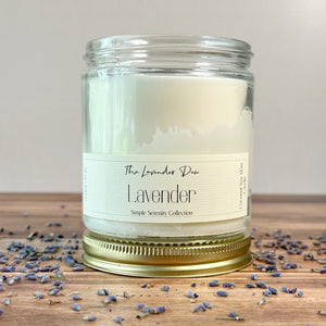 Lavender candle with a label on a wooden surface with lavender petals.