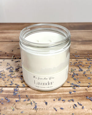Lavender scented candle in a glass jar on a wooden surface with scattered lavender buds.