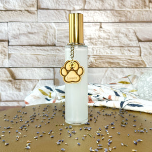 Clear bottle room spray with gold lid and paw print charm on a gold tray and brick background