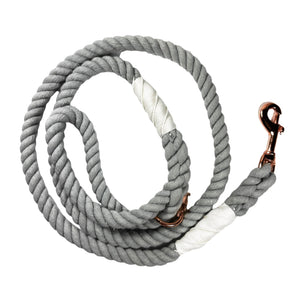 Light gray colored rope dog leash with rose gold hardware and charm coiled up a white background. 