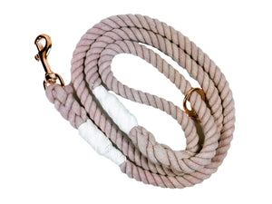 Mauve colored rope dog leash with rose gold hardware and charm coiled up a white background. 