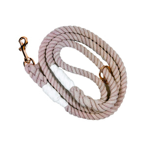Mauve colored rope dog leash with rose gold hardware and charm coiled up a white background. 