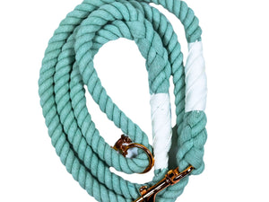 Blue green colored rope dog leash with rose gold hardware and charm coiled up a white background. 