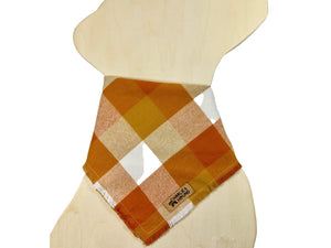 Plaid flannel bandana on a dog-shaped wooden cutout. The plaid fabric has shades of orange, red-orange, and white.