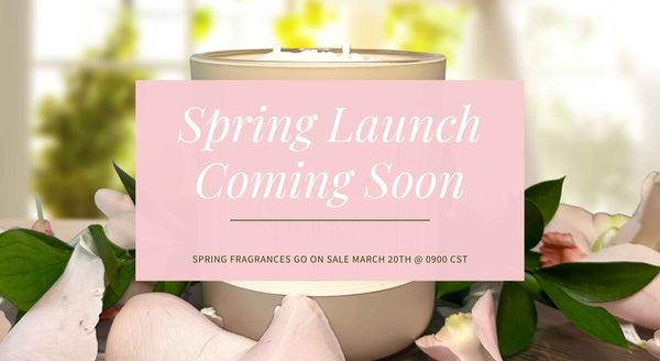 Candle with a 'Spring Launch Coming Soon' sign in front of greenery