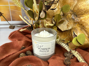 Candle labeled 'Sug's Pumpkin Patch' with decorative fall elements including a gold leaf, green leaves, and a orange fabric.