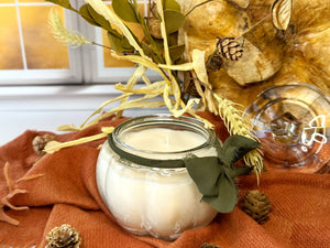 Candle in a pumpkin shaped glass jar with decorative elements on an orange fabric background