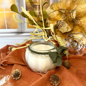 Candle in a pumpkin shaped glass jar with decorative elements on an orange fabric background
