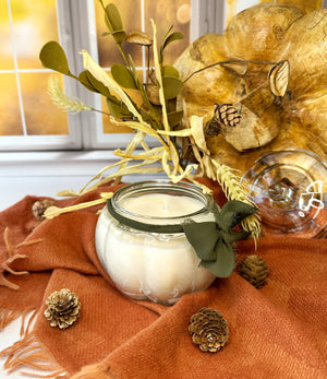 Candle in a pumpkin shaped glass jar with decorative elements on an orange fabric background
