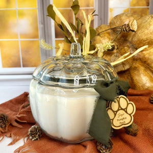 Decorative candle in a pumpkin shaped glass jar with a paw print ribbon on a fall-themed background
