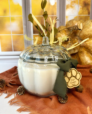 Decorative candle in a pumpkin shaped glass jar with a paw print ribbon on a fall-themed background