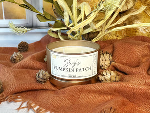Candle labeled 'Sug's Pumpkin Patch' on a textured surface with decorative elements.