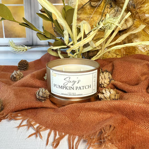 Candle labeled 'Sug's Pumpkin Patch' on a textured surface with decorative elements.