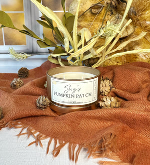 Candle labeled 'Sug's Pumpkin Patch' on a textured surface with decorative elements.