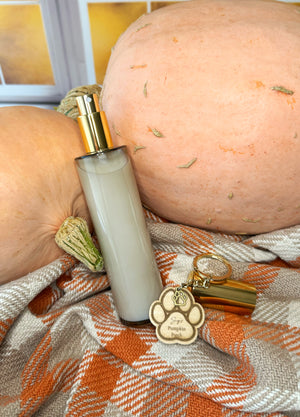 Room spray bottle with gold sprayer and decorative tag on a plaid fabric with pumpkins in the background.