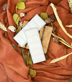 Two white wax melt bars on an orange fabric background with decorative elements.
